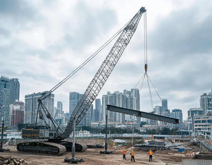 Crawler crane lifting steel beam on urban construction site